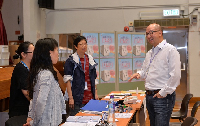 Photo shows Mr Tam (first right) chatting with staff at the polling station.
